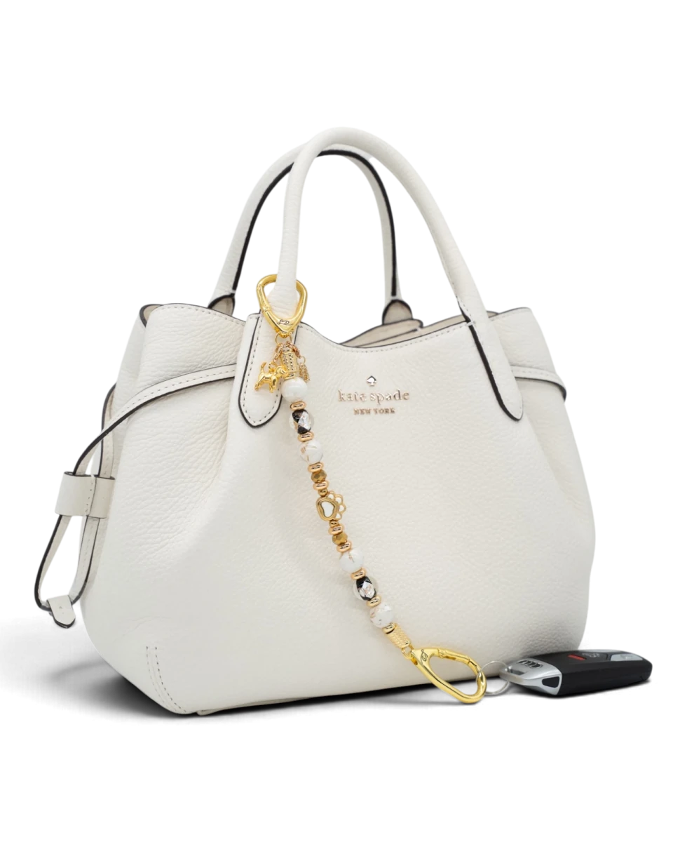 LD Keyfinder Furever Love beaded keychain with gold paw charm and white seashell beads attached to a white handbag.