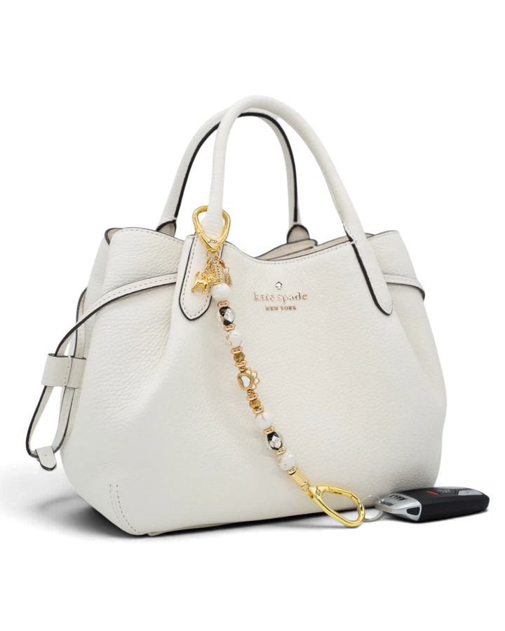 LD Keyfinder Furever Love beaded keychain with gold paw charm and white seashell beads attached to a white handbag.