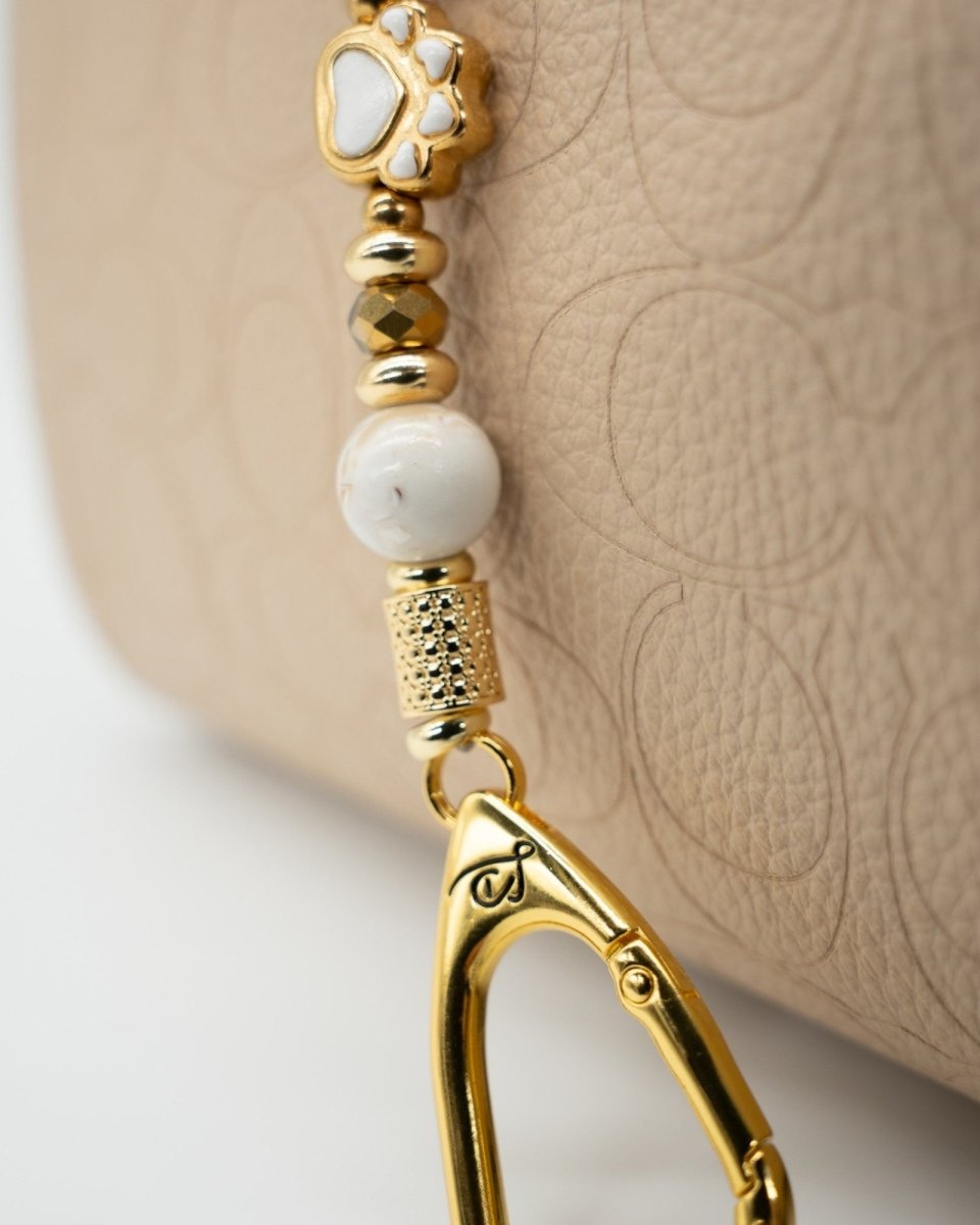 LD Keyfinder Furever Love-Mini featuring white enamel paw bead, gold-plated charms, and seashell beads on a handbag.