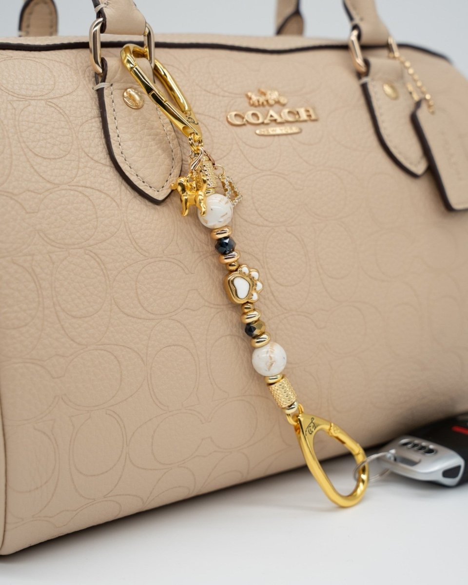 LD Keyfinder Furever Love-Mini featuring white seashell beads, gold paw charm, and heart charm on a beige handbag.