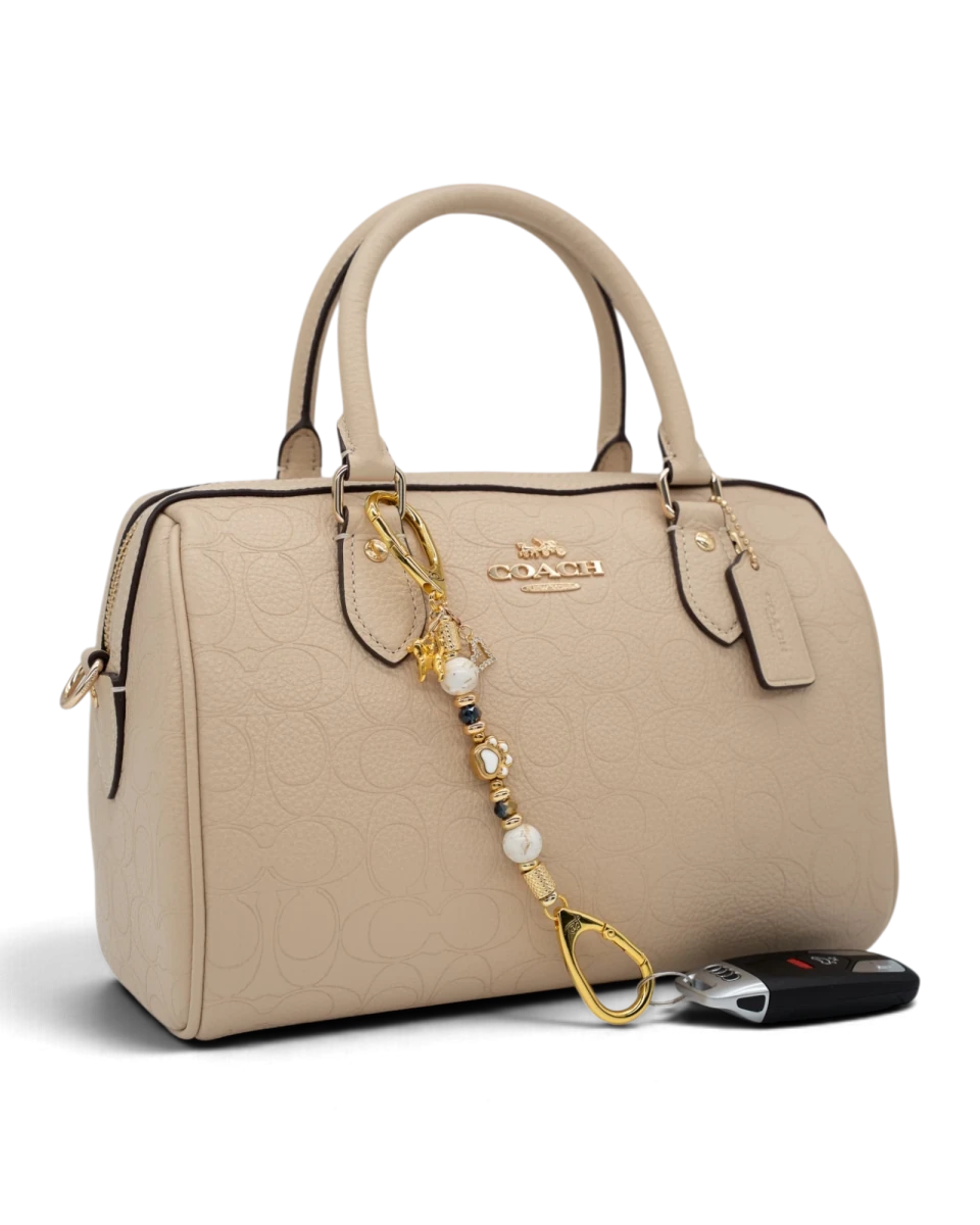 LD Keyfinder Furever Love-Mini attached to a beige Coach handbag, featuring white seashell and gold-plated dog charms.