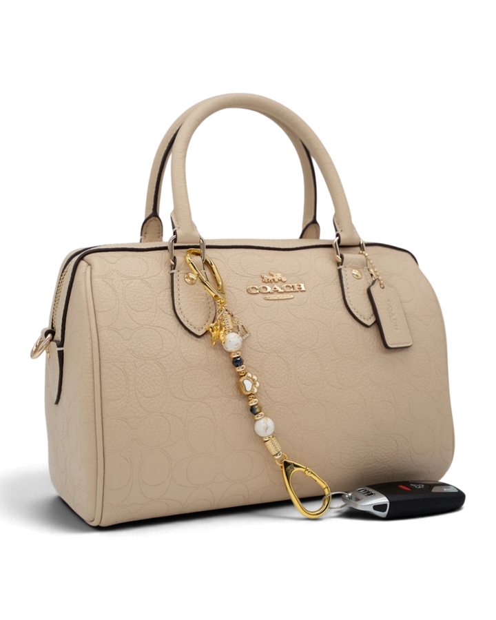 LD Keyfinder Furever Love-Mini attached to a beige Coach handbag, featuring white seashell and gold-plated dog charms.