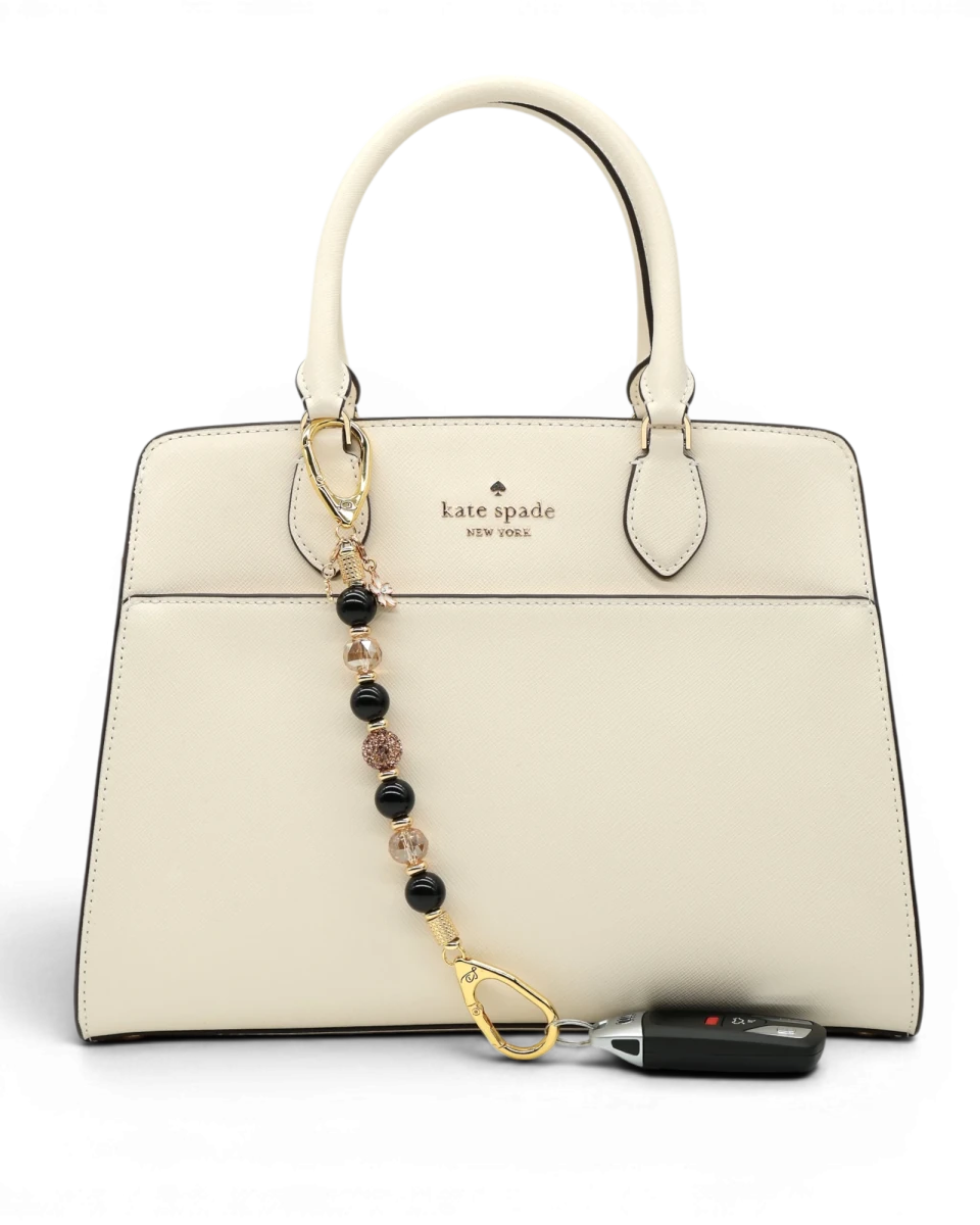 LD Keyfinder Gilded Bee charm with black obsidian, gold crystal beads, flower and bee charms attached to a cream handbag.