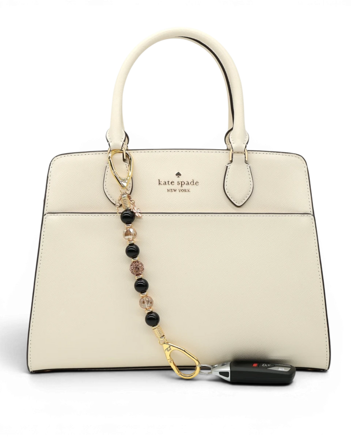 LD Keyfinder Gilded Bee charm with black obsidian, gold crystal beads, flower and bee charms attached to a cream handbag.