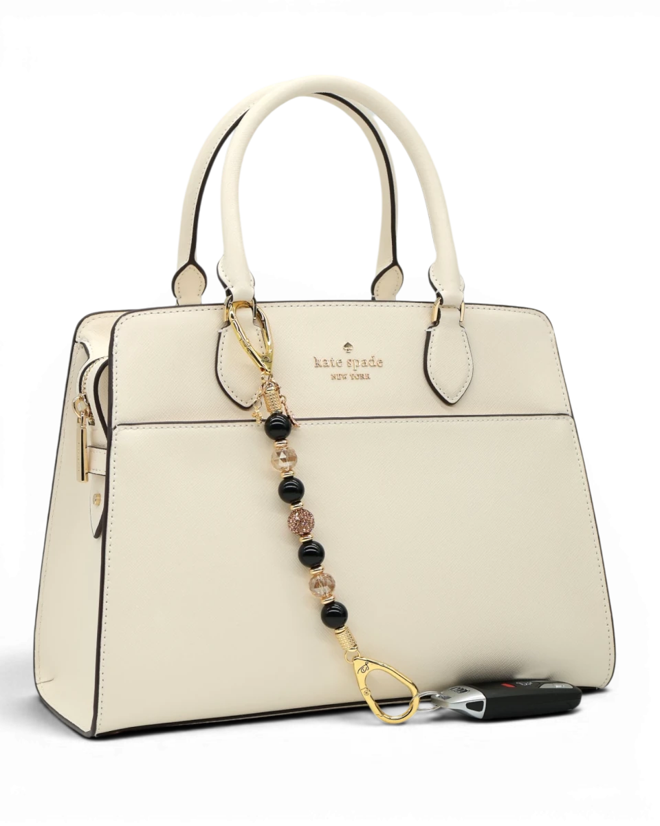 LD Keyfinder Gilded Bee keychain with black obsidian, gold crystal beads, and bee charm attached to a cream handbag.