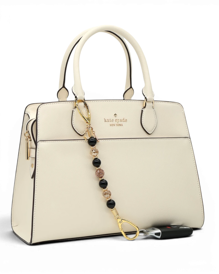 LD Keyfinder Gilded Bee keychain with black obsidian, gold crystal beads, and bee charm attached to a cream handbag.