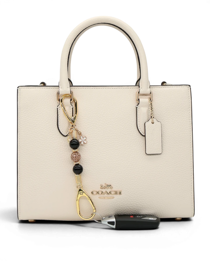 LD Keyfinder Gilded Bee Mini keychain with black obsidian beads, crystal accents, and flower & bee charms on a cream handbag.