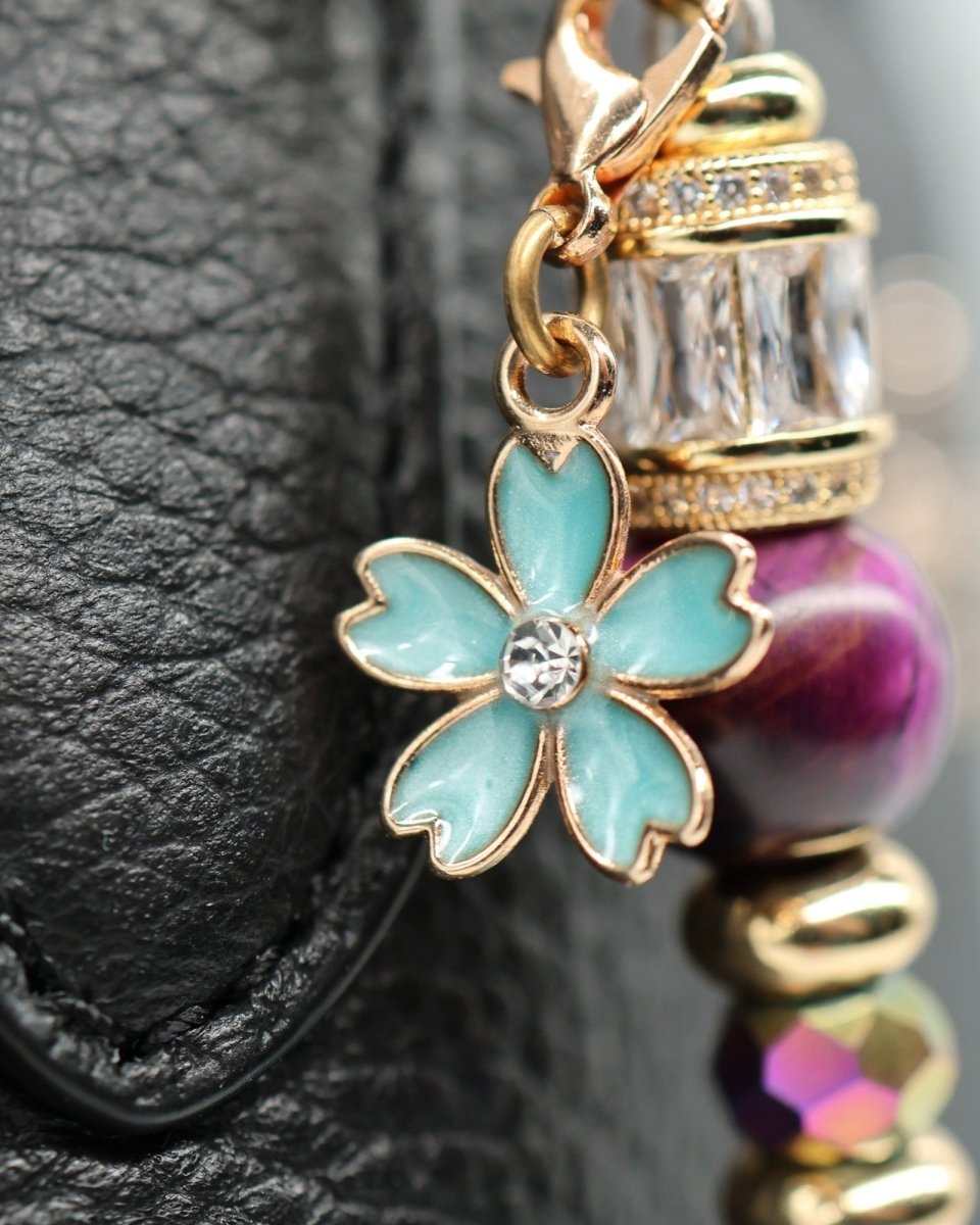LD Keyfinder Gilded Fantasy charm with blue enamel flower, purple tiger eye, gold beads, and rhinestones on black leather.