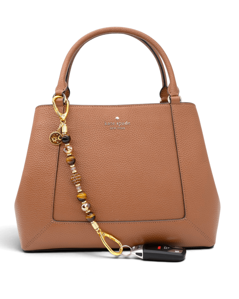 LD Keyfinder Golden Equinox beaded accessory with Tiger Eye and gold charms attached to a brown leather handbag