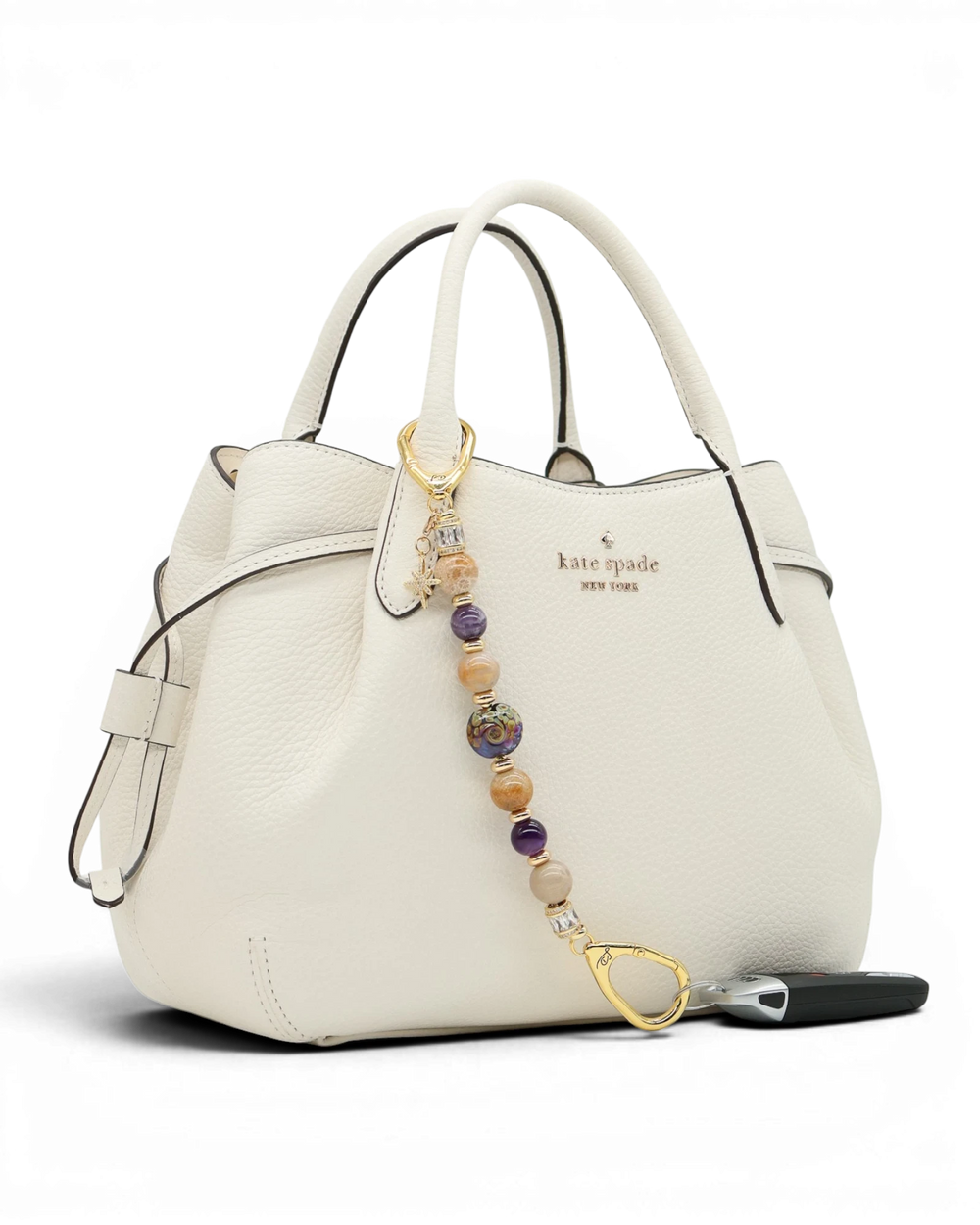 LD Keyfinder Golden Nebula charm with purple, gold, and amethyst beads, gold-plated star charm on white handbag.