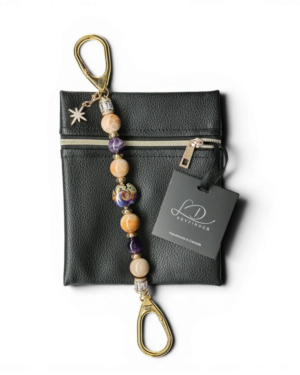 LD Keyfinder Golden Nebula keychain with purple, gold, and tan beads, a glass focal bead, and a star charm. Includes a black vegan leather pouch.