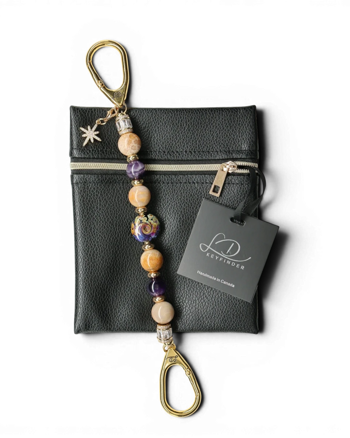 LD Keyfinder Golden Nebula keychain with purple, gold, and tan beads, a glass focal bead, and a star charm. Includes a black vegan leather pouch.