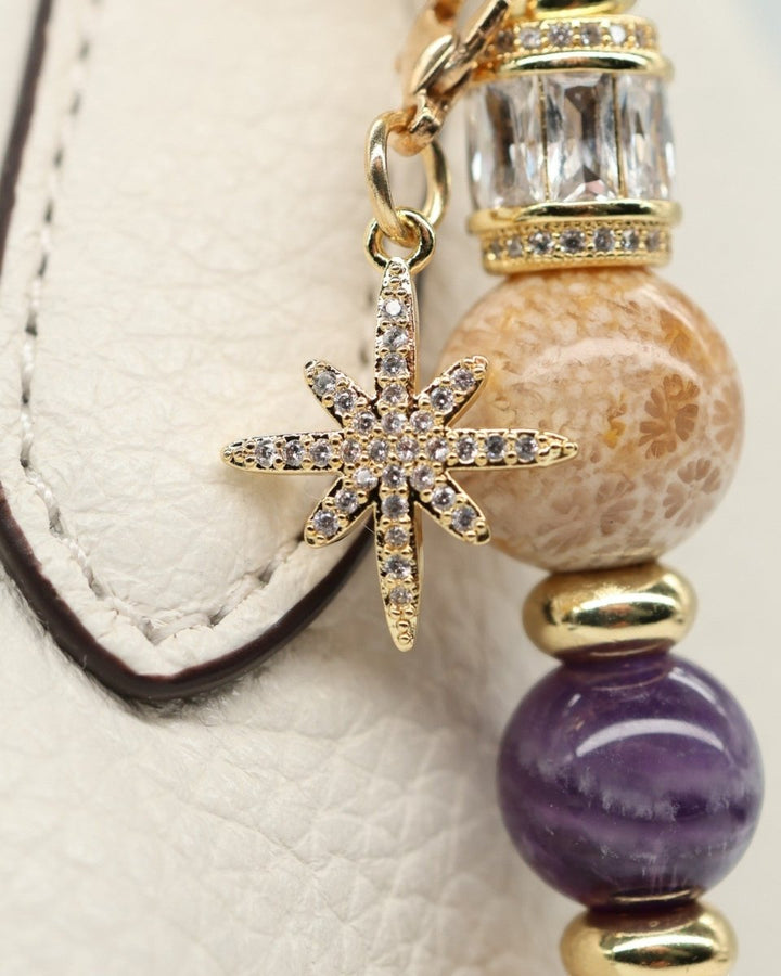 LD Keyfinder Golden Nebula charm with fossil coral, amethyst, gold spacers, and pavé star charm on a white textured surface.