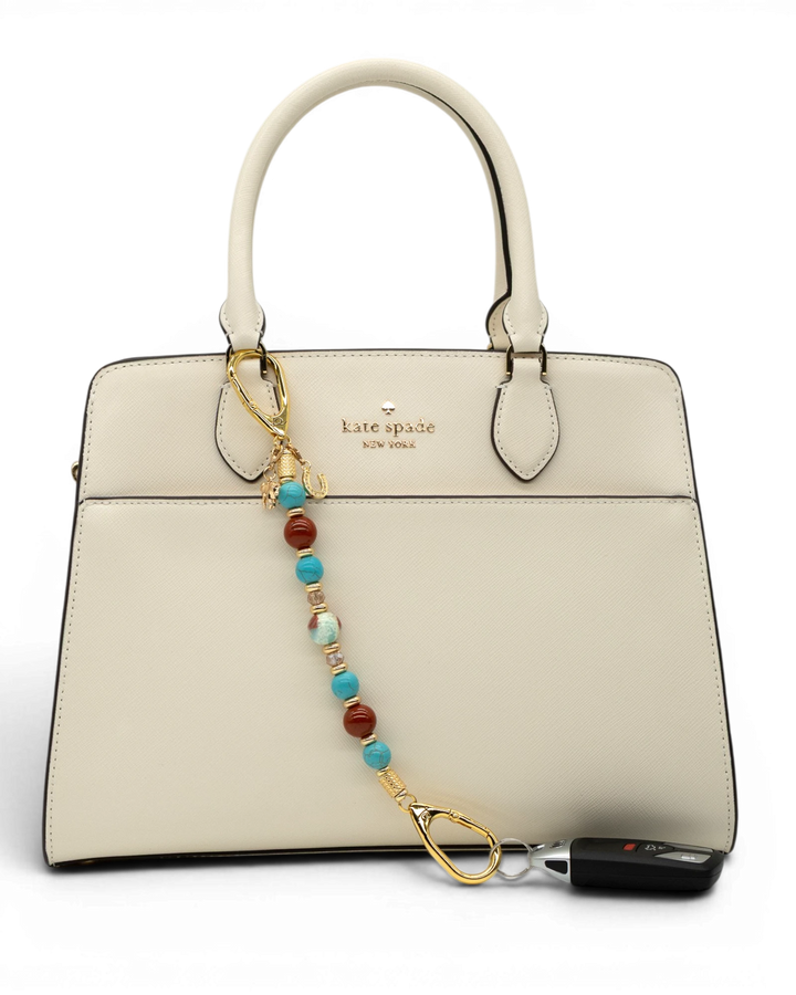 LD Keyfinder Golden Prairie beaded accessory with turquoise, red jasper, and gold charms attached to a white handbag.