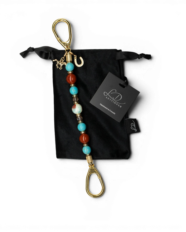 LD Keyfinder Golden Prairie beaded keychain with turquoise, red jasper, and gold charms on a black velvet pouch.
