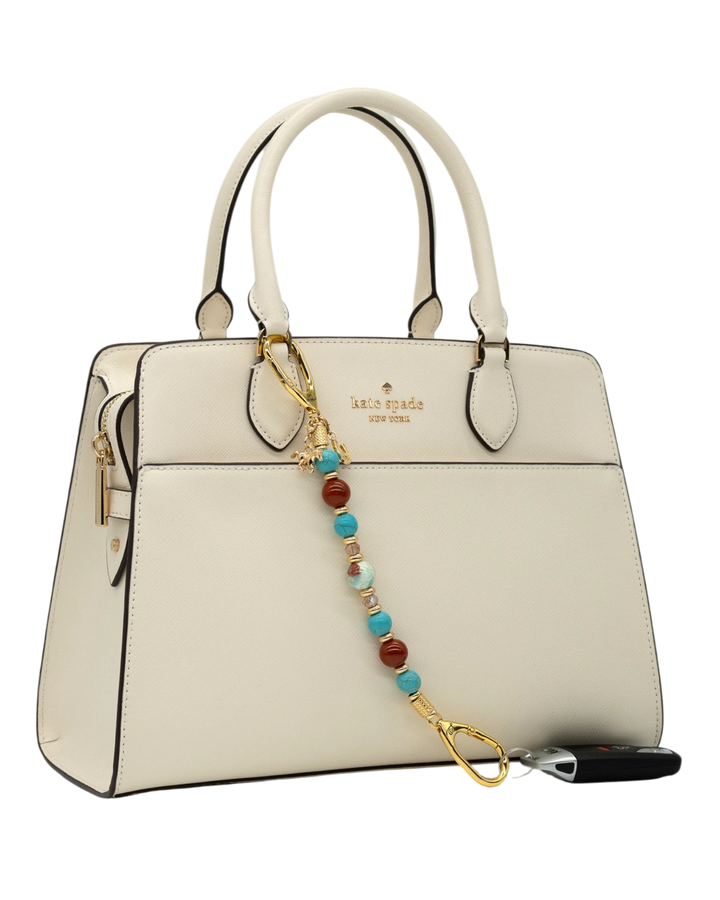 LD Keyfinder Golden Prairie beaded accessory with turquoise, red jasper, and gold charms attached to a white handbag.