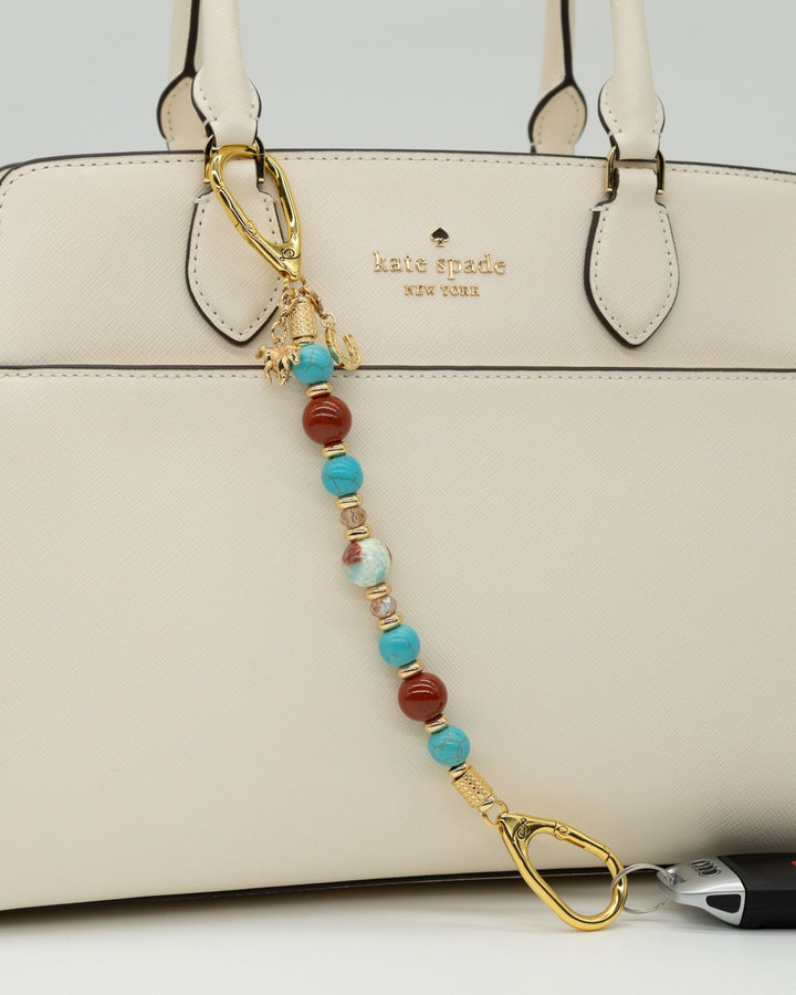 LD Keyfinder Golden Prairie beaded keychain with turquoise, red jasper, and gold charms attached to a white handbag.