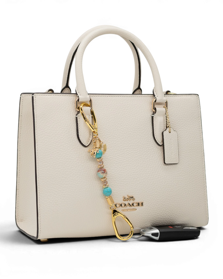 LD Keyfinder Golden Prairie-Mini beaded charm with turquoise and gold accents attached to a white leather handbag.