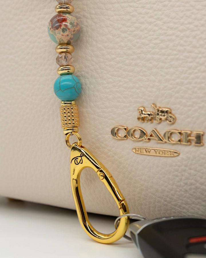 LD Keyfinder Golden Prairie Mini beaded keychain with turquoise, jasper, and gold charms attached to a white handbag.