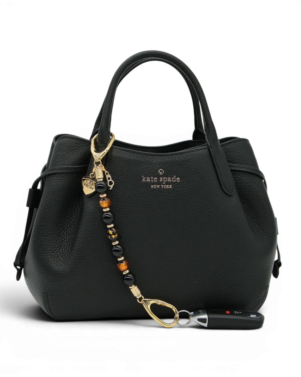 LD Keyfinder Golden Purrs beaded key accessory with black obsidian and gold foil cat charms attached to a black bag.