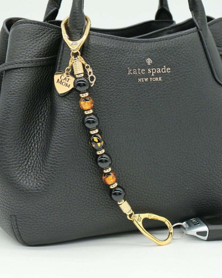 LD Keyfinder Golden Purrs beaded keychain with black obsidian, gold foil lampwork beads, and cat charms on a black bag