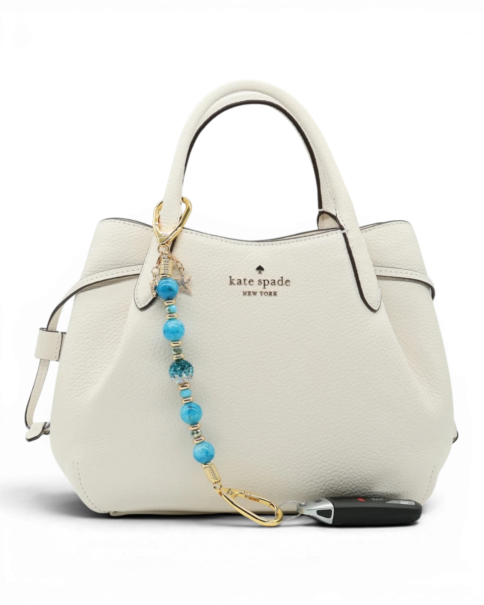 LD Keyfinder Golden Reef keychain with aqua hemimorphite beads, Austrian crystal, gold-plated charms, and keys attached to a white handbag.