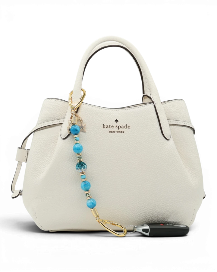 LD Keyfinder Golden Reef keychain with aqua hemimorphite beads, Austrian crystal, gold-plated charms, and keys attached to a white handbag.