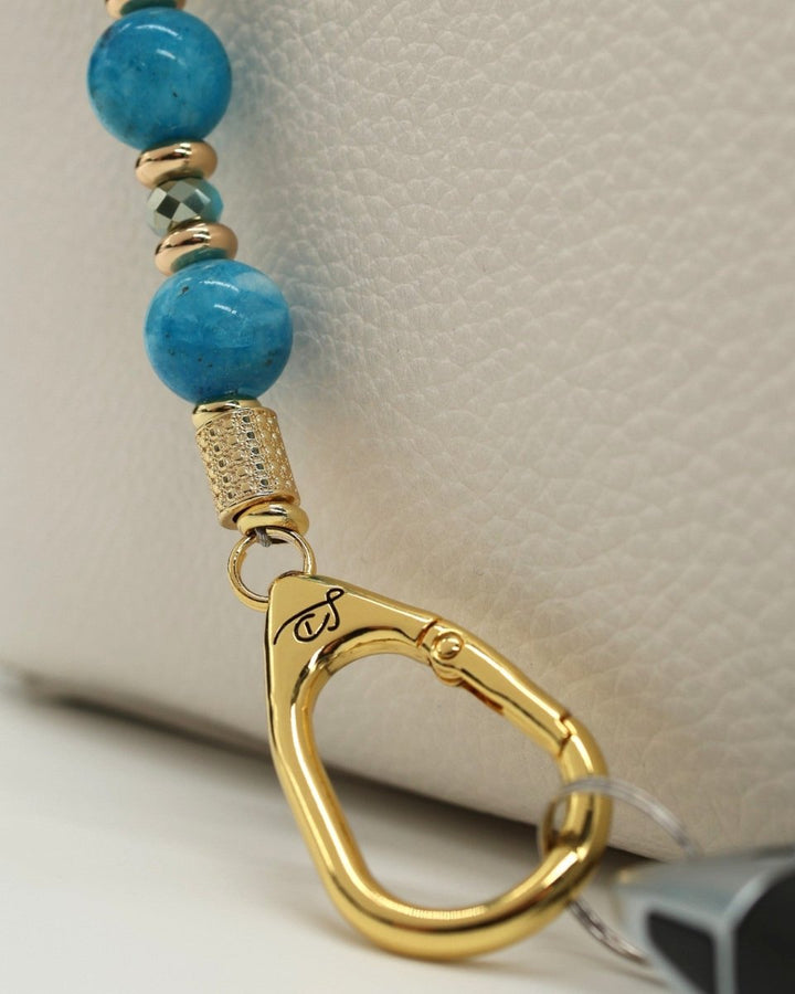 LD Keyfinder Golden Reef bracelet with aqua hemimorphite beads, gold accents, and charms on a light-colored textured surface.