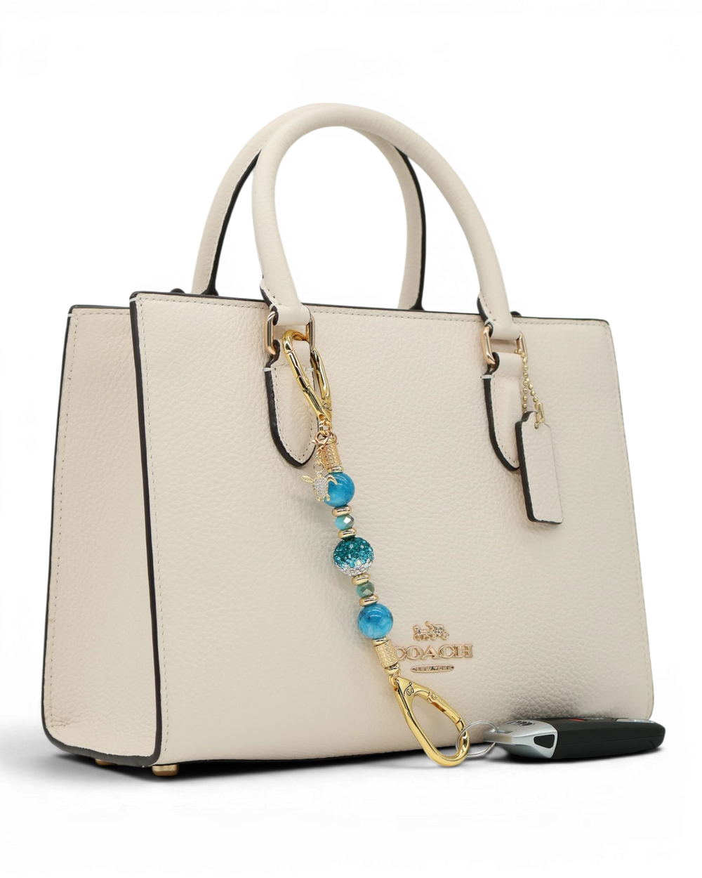 LD Keyfinder Golden Reef Mini charm with aqua hemimorphite beads, crystal, starfish, and sea turtle charms on a cream handbag.