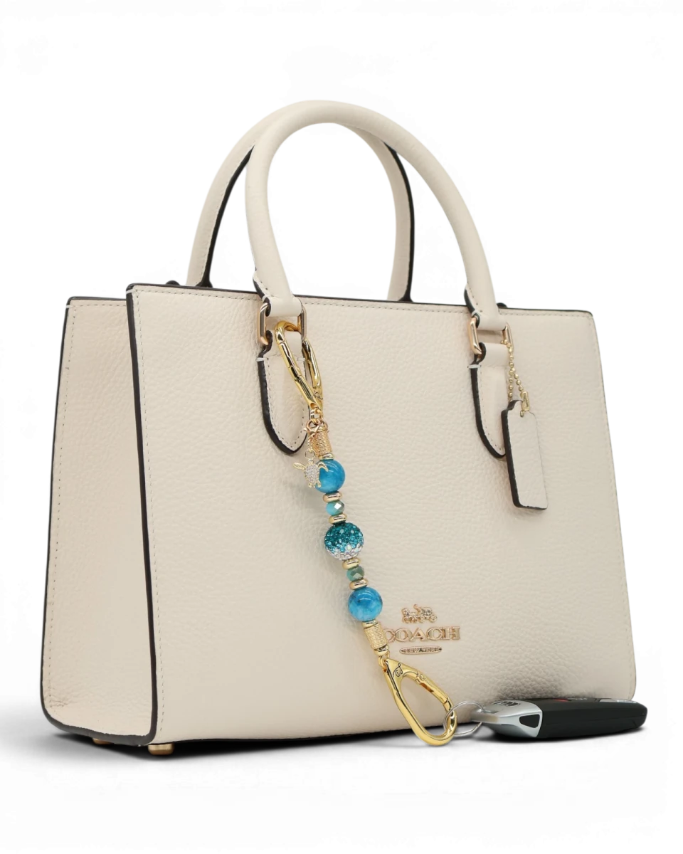 LD Keyfinder Golden Reef Mini charm with aqua hemimorphite beads, crystal, starfish, and sea turtle charms on a cream handbag.