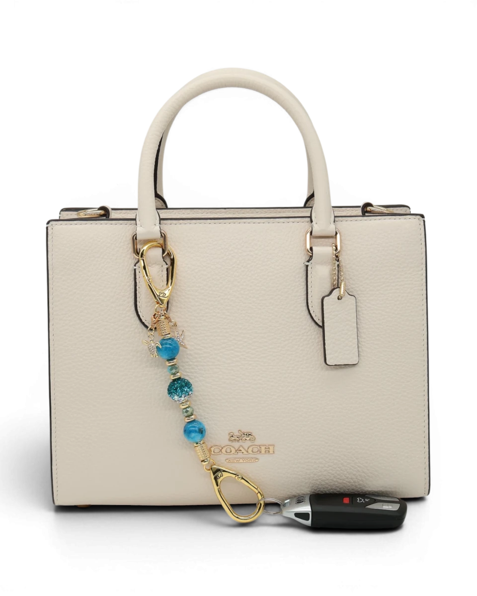 LD Keyfinder Golden Reef Mini keychain with aqua hemimorphite beads, crystal, starfish, and sea turtle charms, attached to a cream handbag.