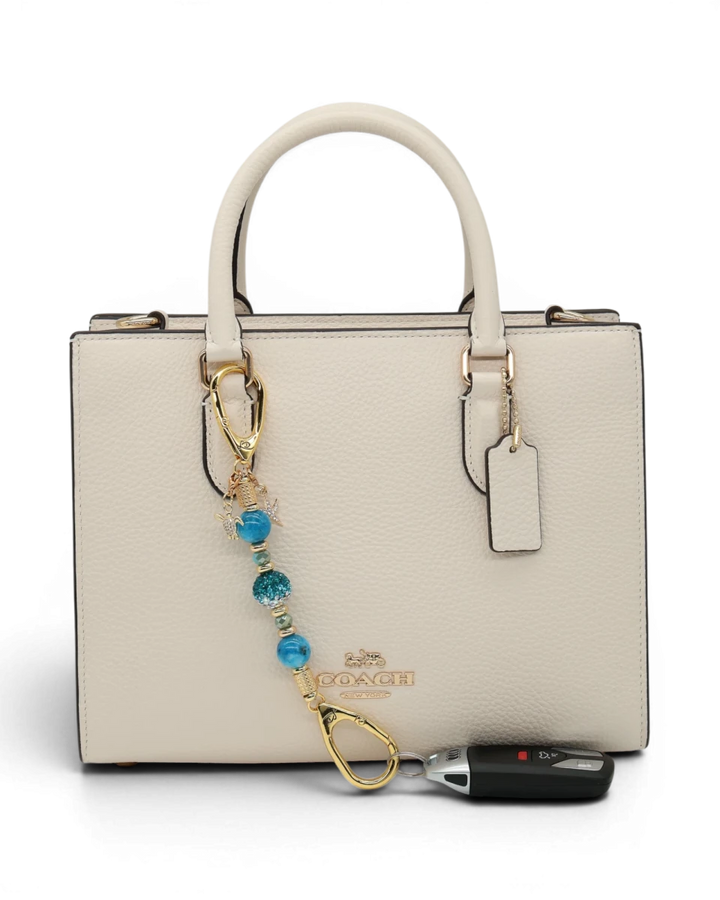 LD Keyfinder Golden Reef Mini keychain with aqua hemimorphite beads, crystal, starfish, and sea turtle charms, attached to a cream handbag.