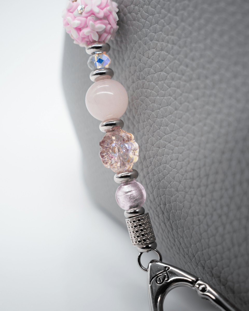 LD Keyfinder Hope Blooms keychain featuring pink rose quartz, glass flower beads, and iridescent crystals on a grey bag.