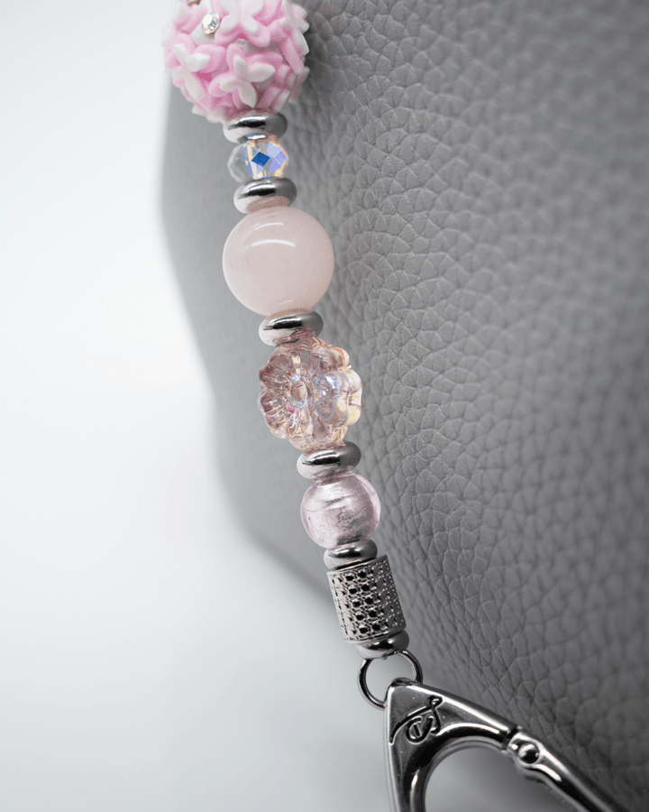 LD Keyfinder Hope Blooms keychain featuring pink rose quartz, glass flower beads, and iridescent crystals on a grey bag.