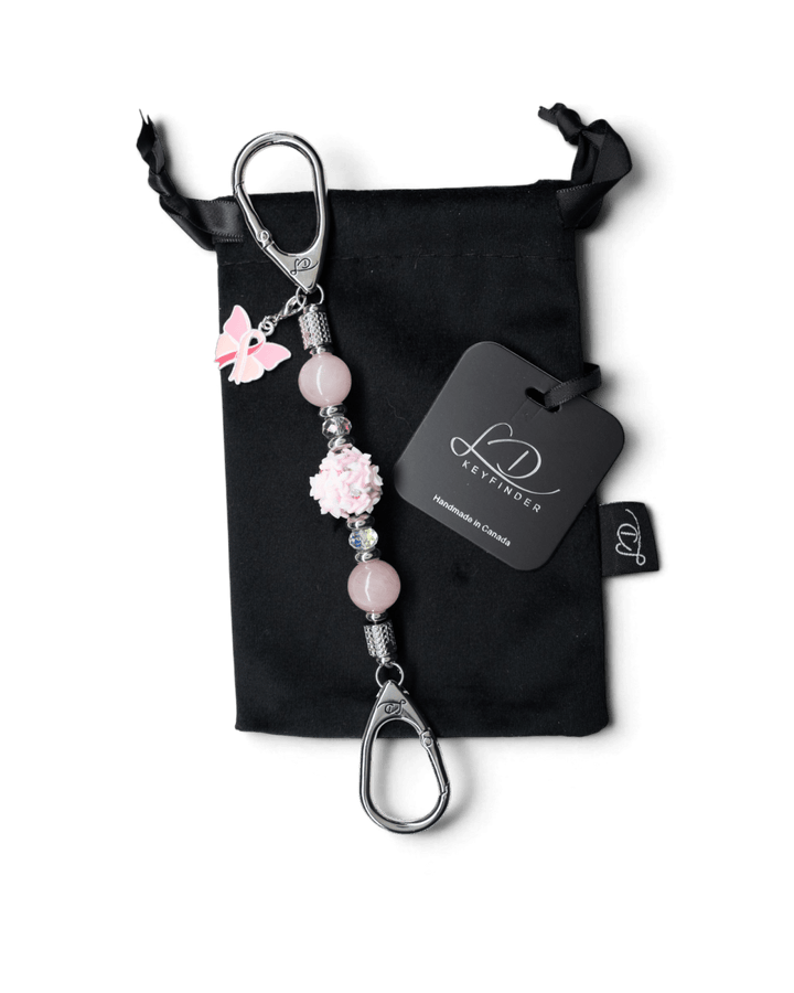 LD Keyfinder Hope Blooms Mini with rose quartz beads, clay butterfly, and pink ribbon charm on a black velvet bag.