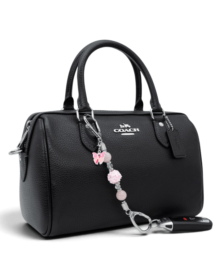 LD Keyfinder Hope Blooms-Mini attached to a black handbag, featuring rose quartz, crystal beads, and a pink ribbon charm