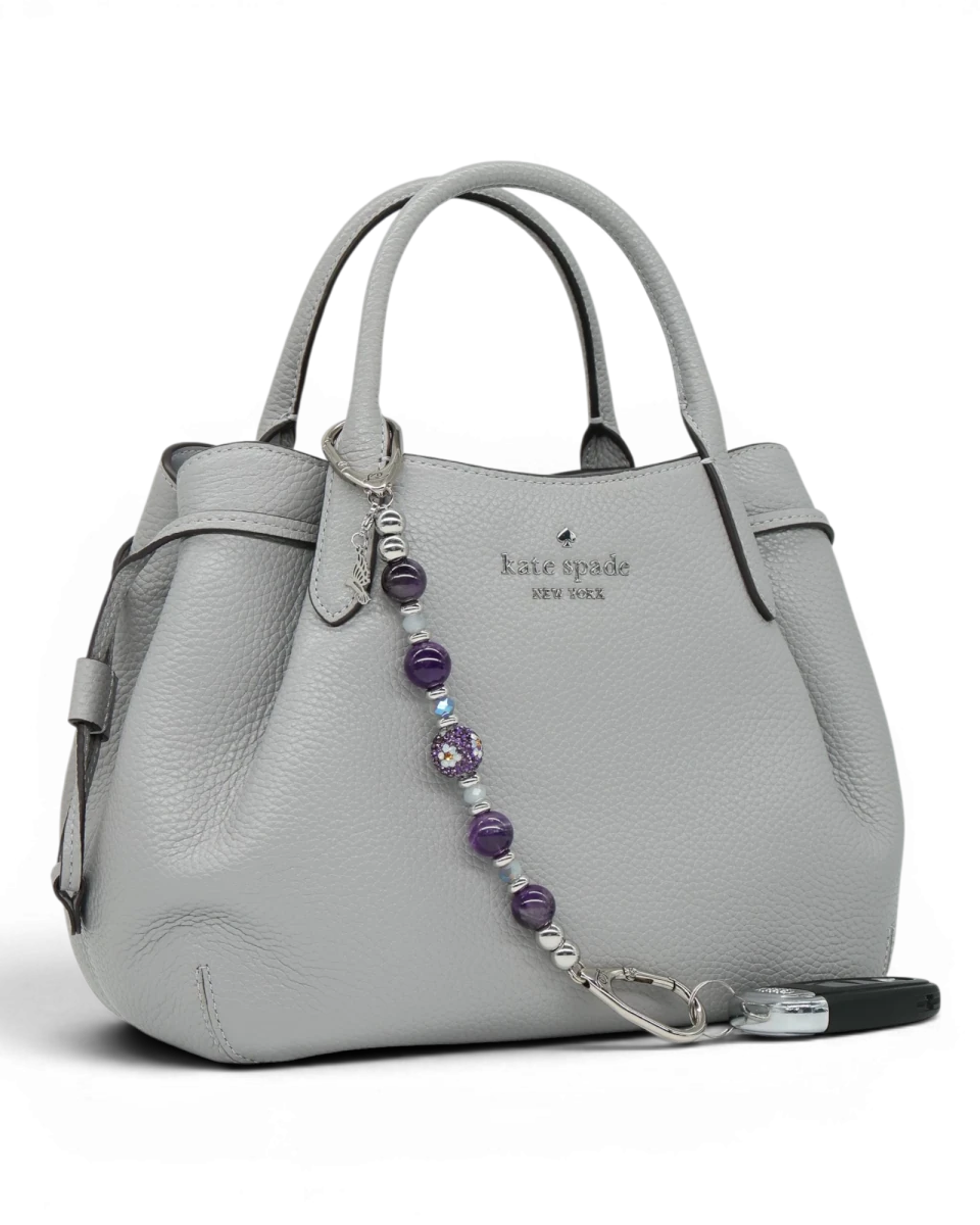 LD Keyfinder Hummingbird Dream keychain with amethyst, glass beads, and hummingbird charm attached to a grey handbag.