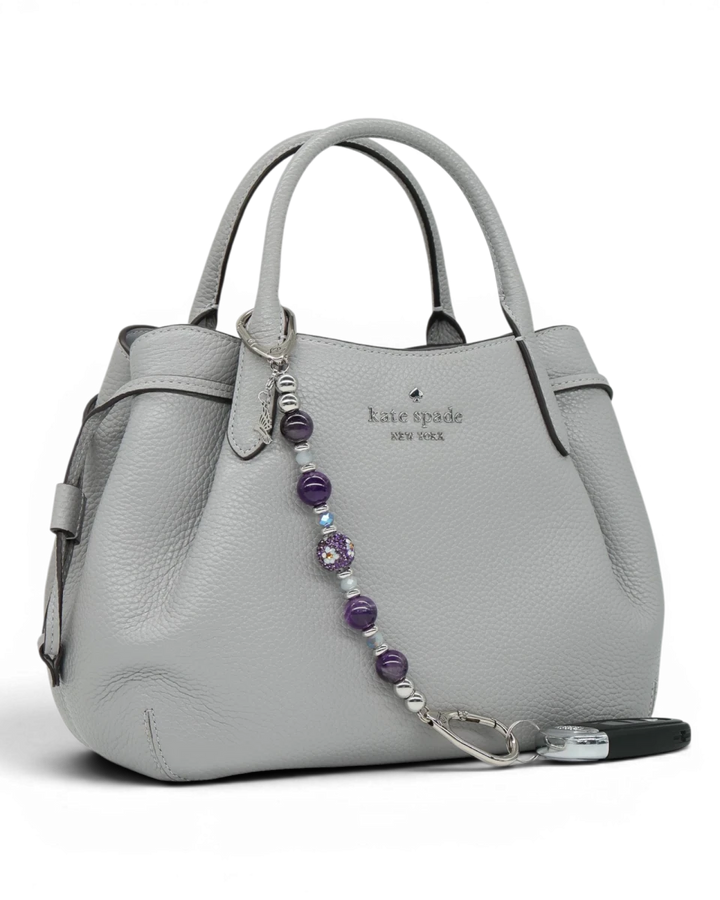 LD Keyfinder Hummingbird Dream keychain with amethyst, glass beads, and hummingbird charm attached to a grey handbag.