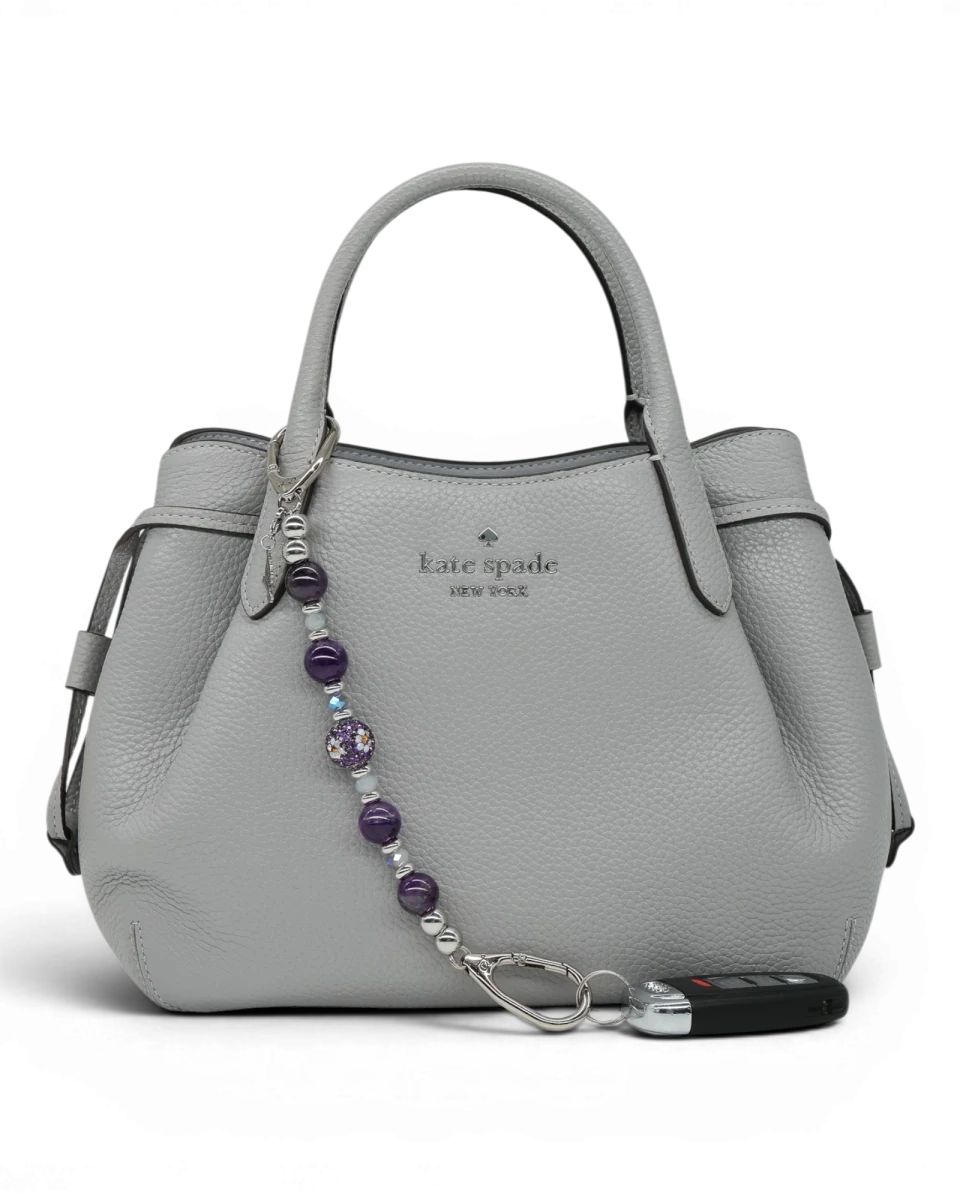 LD Keyfinder Hummingbird Dream charm with amethyst, jade glass beads, and hummingbird charm on a grey handbag.
