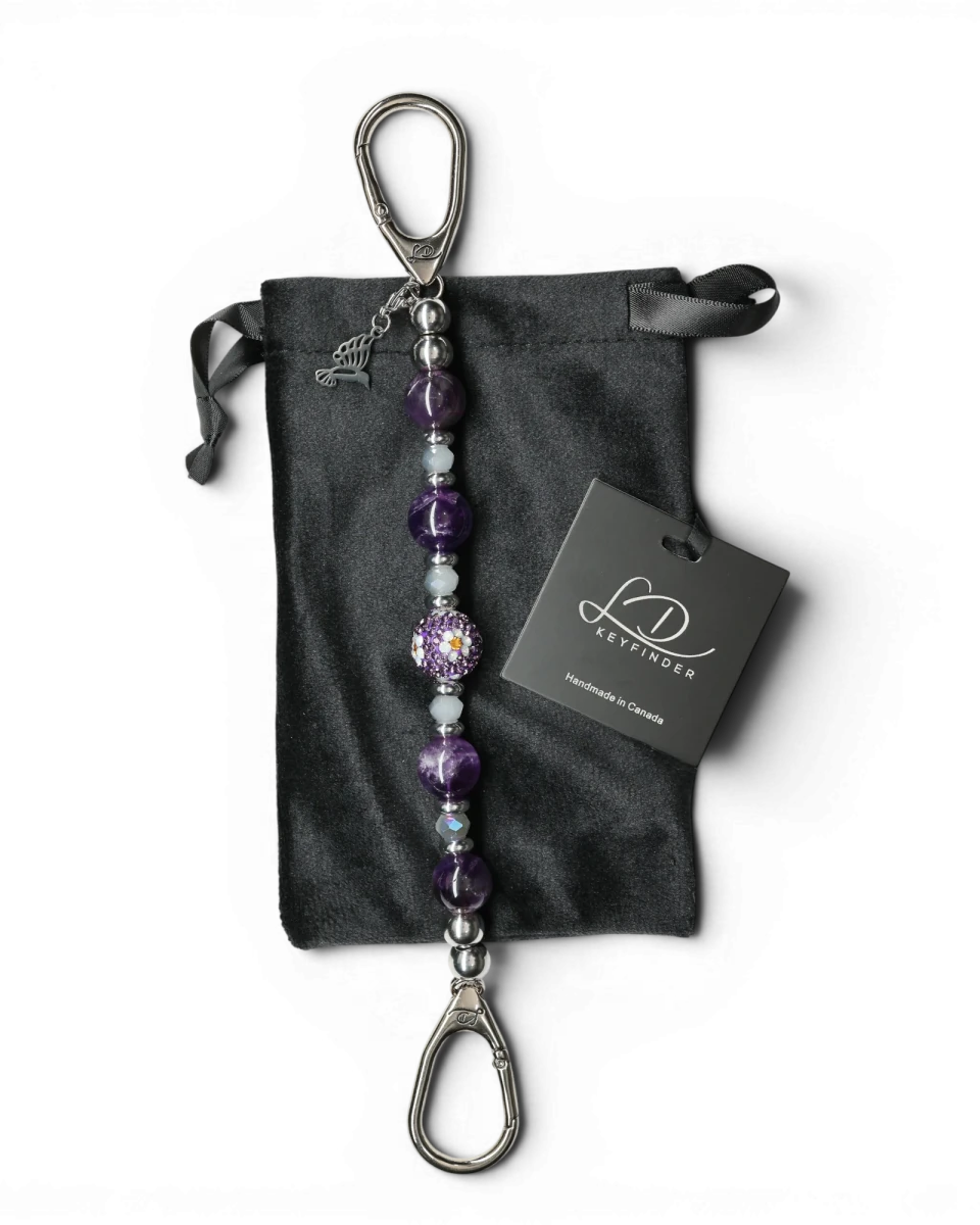 LD Keyfinder Hummingbird Dream keychain with amethyst, crystal daisy bead, and hummingbird charm on black velvet bag.