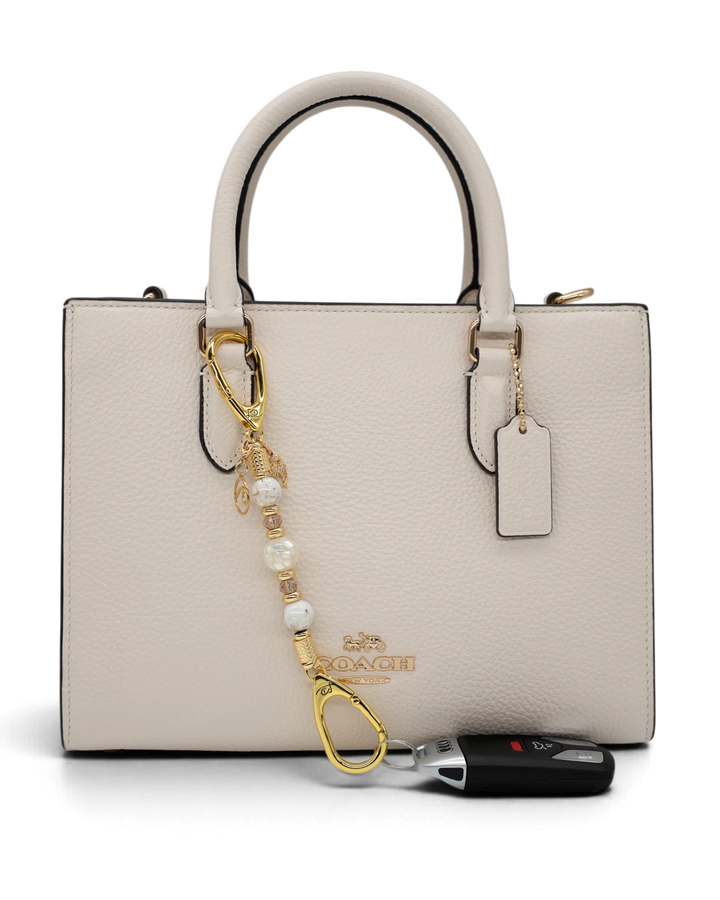 LD Keyfinder Mediterranean Glow-Mini attached to a cream leather handbag with pearl, gold, and dolphin charms