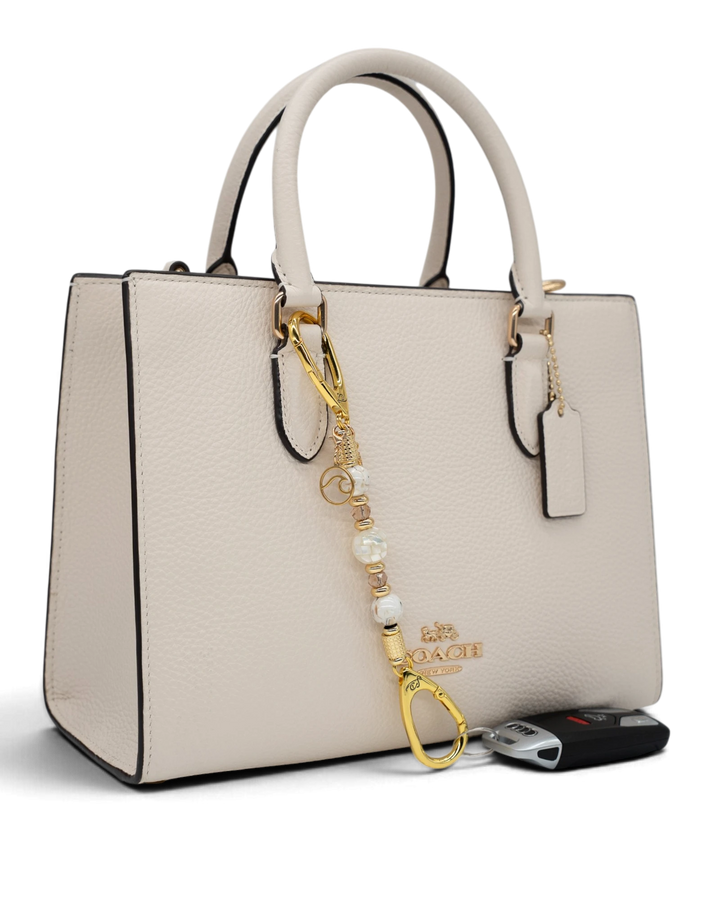 LD Keyfinder Mediterranean Glow Mini featuring Mother of Pearl, ivory shell beads, and gold charms on a cream handbag