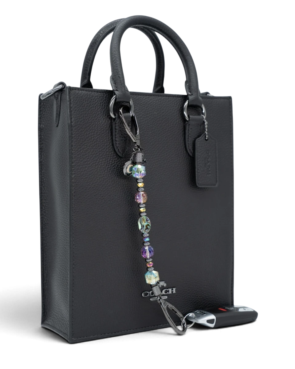 LD Keyfinder Midnight Aurora beaded keychain with abalone shell, rainbow crystals, and moon charm on a black handbag.