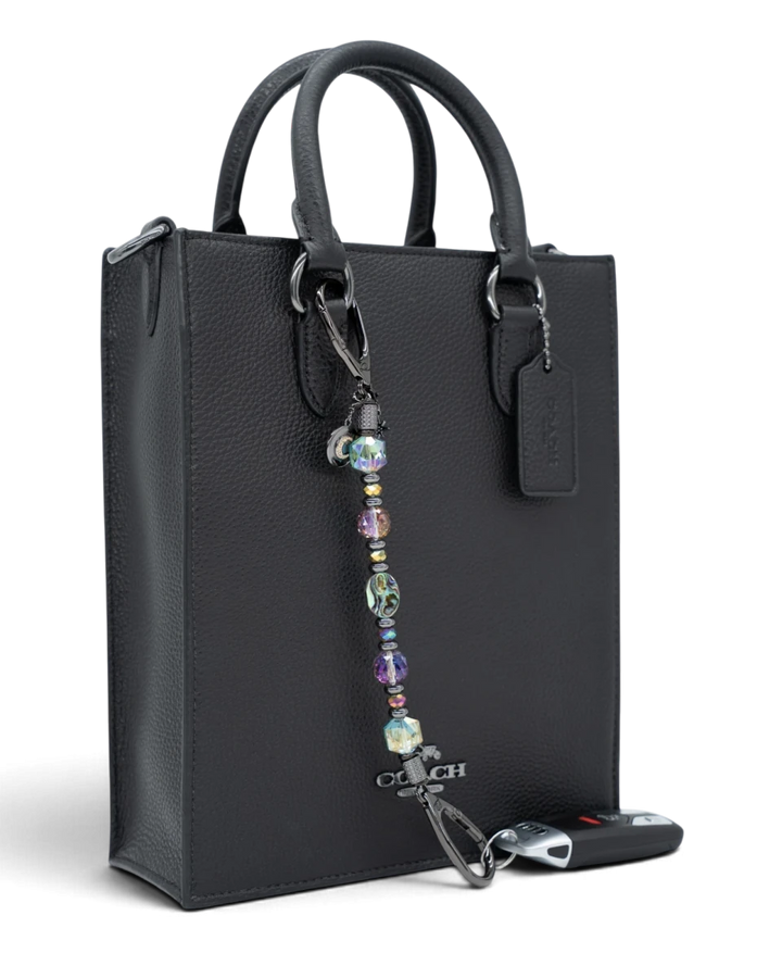 LD Keyfinder Midnight Aurora beaded keychain with abalone shell, rainbow crystals, and moon charm on a black handbag.