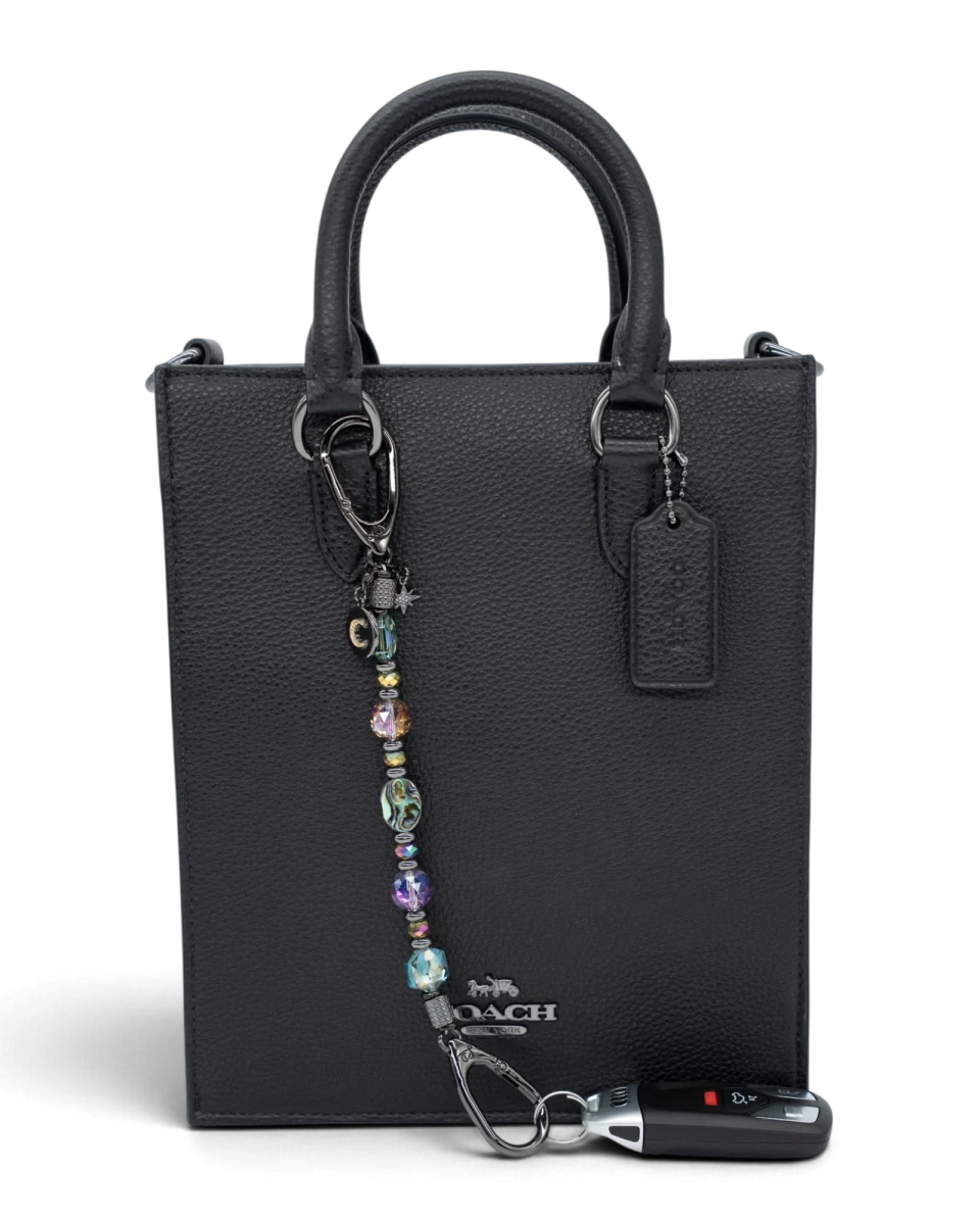 LD Keyfinder Midnight Aurora beaded keychain with abalone shell and rainbow crystals attached to a black leather bag.