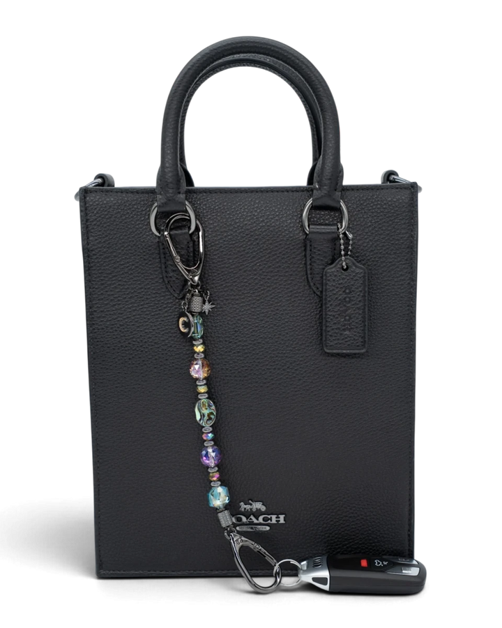 LD Keyfinder Midnight Aurora beaded keychain with abalone shell and rainbow crystals attached to a black leather bag.