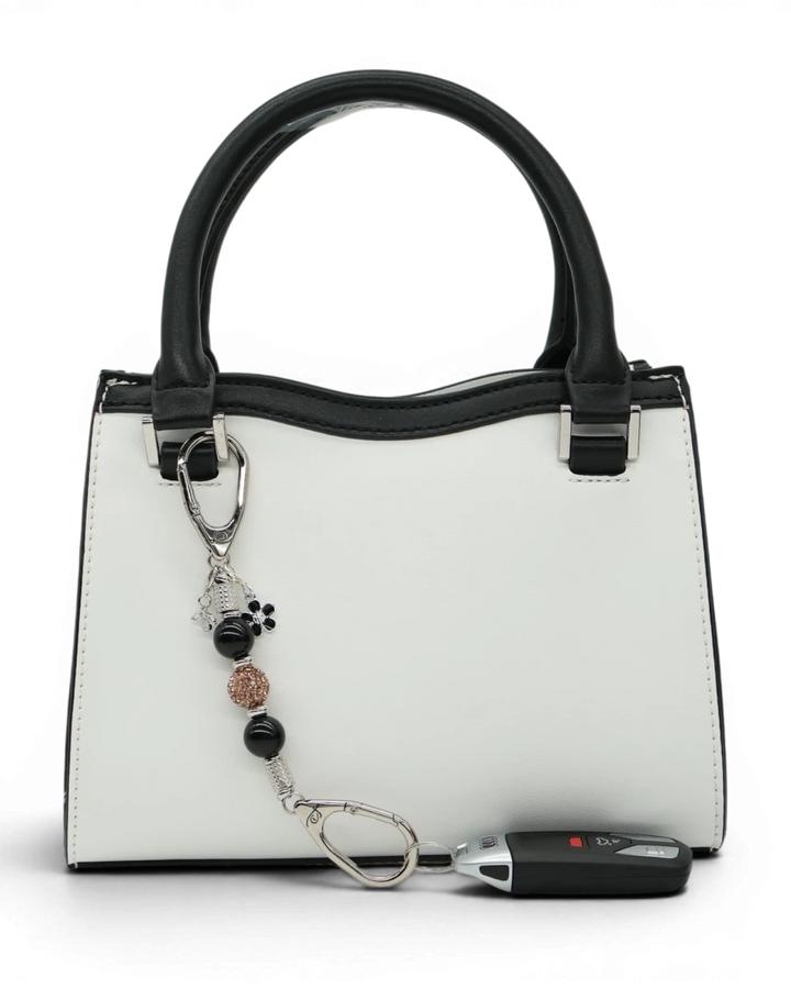 LD Keyfinder Midnight Hive Mini keychain with black obsidian beads, crystal charm, bumblebee, and flower charm attached to a white handbag.