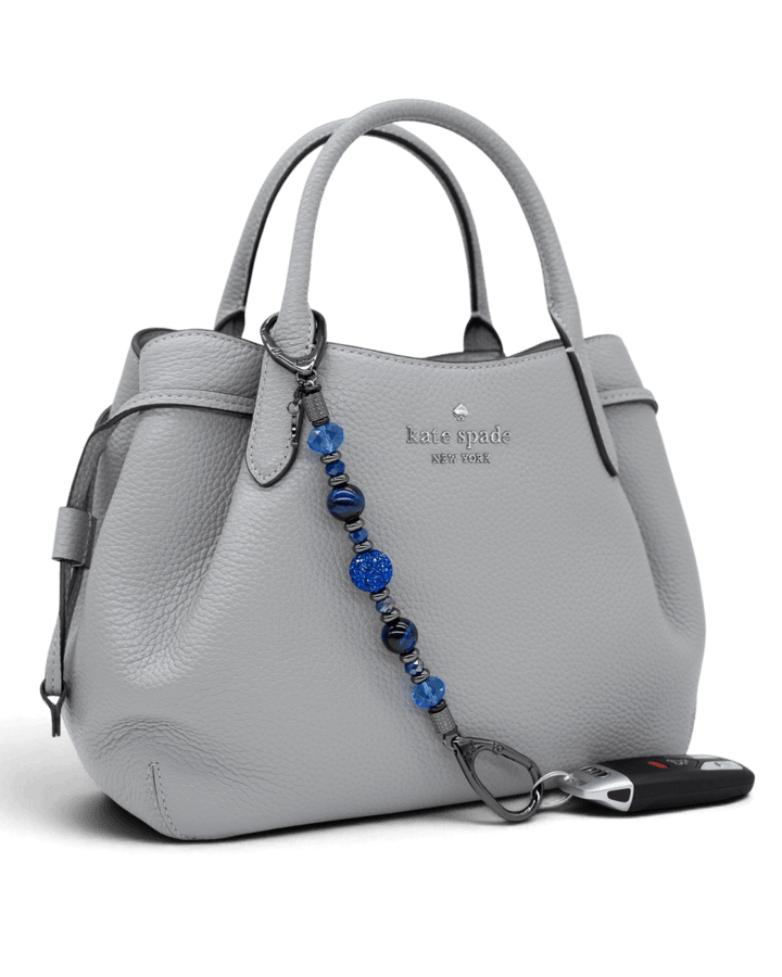 LD Keyfinder Midnight Sapphire beaded accessory with blue tiger eye and crystal charms attached to a grey handbag