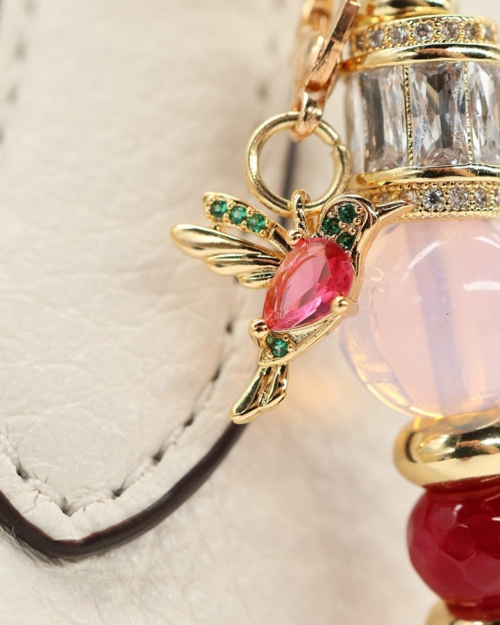 LD Keyfinder Opalite Bloom charm with hummingbird, pink opalite, ruby, and gold accents on a white textured surface.