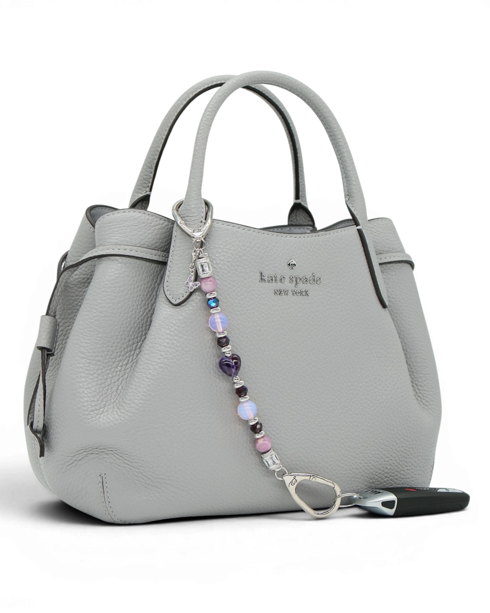 LD Keyfinder Orchid Flutter beaded accessory with lepidolite, opalite, and butterfly charm attached to a grey handbag.